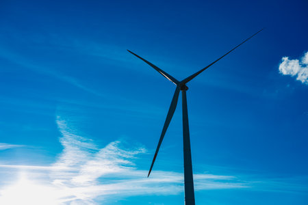 A striking view of a turbine wind rises against a deep blue sky filled with wispy clouds. Sunlight glimmers, creating an inspiring scene of renewable energy and nature coexist.の写真素材