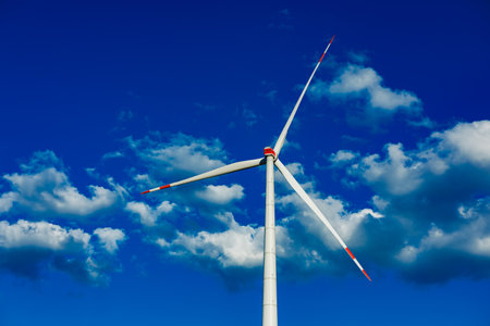 A striking wind turbine rises prominently against a bright blue sky, surrounded by soft, white...