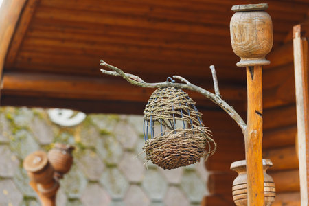 A charming handmade birdhouse is suspended from a wooden post in a rustic outdoor area, showing intricate weaving and natural materials under bright daylight.の写真素材