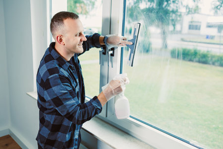 A man happily cleans a large window with a squeegee, using a spray bottle to ensure a clear view...