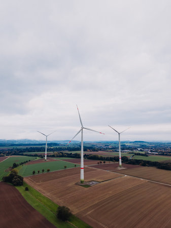Wind turbines stand tall against a gray sky, their blades slowly turning.の写真素材