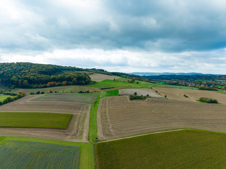 Vast green fields stretch across the landscape, bordered by gentle hills and a thick tree line. The...