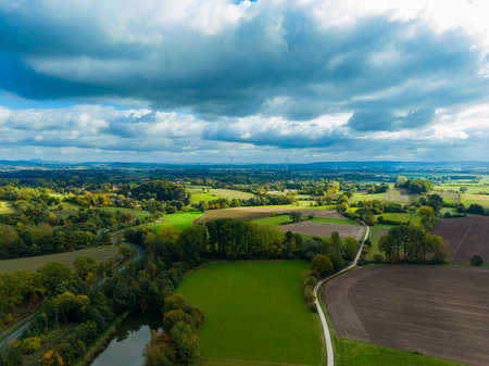 Vibrant green fields stretch across the horizon under a dramatic sky as fluffy clouds float above, capturing the essence of rural tranquility in a serene autumn afternoon.の写真素材