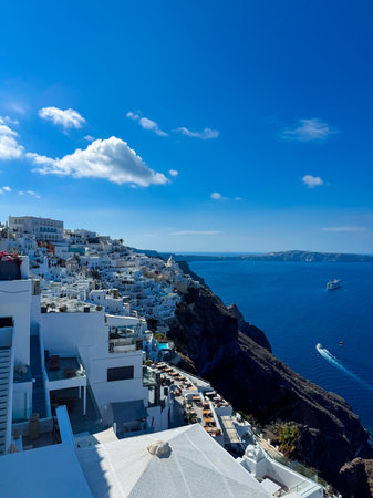 Stunning cliffs rise above the sparkling Aegean Sea, dotted with charming white buildings under a clear blue sky, while boats glide peacefully on the water.の写真素材