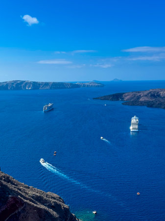 ships Cruise glide peacefully across the deep blue waters of Santorini's caldera, where rocky shores meet the horizon under a bright sky. The balmy atmosphere invites daydreaming.の写真素材