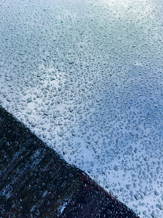 Tiny droplets of rain sit on a metallic surface, showing a beautiful pattern as the sun peeks through layered clouds in the morning sky.の写真素材