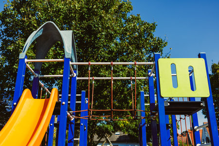 Colorful playground equipment features a bright orange slide and climbing bars against a backdrop of...