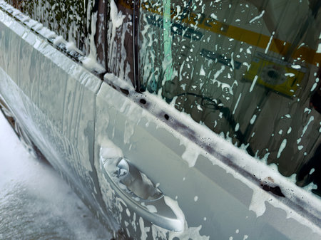 Bubbles and foam cover a silver car in a cheerful car wash, sunlight glinting off the soapy surfaces, revealing a moment of joy and cleanliness during a warm afternoon.の写真素材