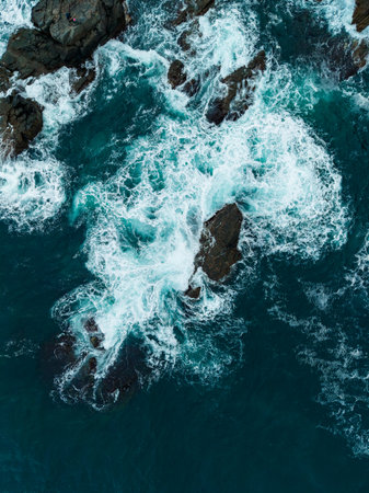 Turbulent waves collide with jagged rocks along the coast, creating a stunning display of water and...