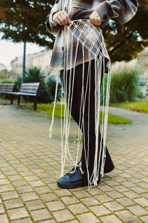A person showcases a handmade macrame belt featuring detailed knots and flowing strands while...