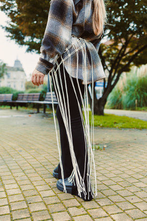A person stands in an urban park wearing a stylish outfit that features intricate fringe detailing,...