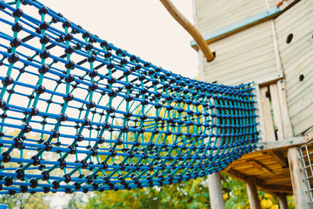 Children play and explore on a colorful rope bridge at a lively playground, bright sunshine illuminating the scene as laughter fills the air among tall trees.の写真素材