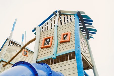 A vibrant playground features a tall structure resembling a small house, with unique windows and a blue slide. Children are drawn to this playful design, enjoying their time outside.の写真素材