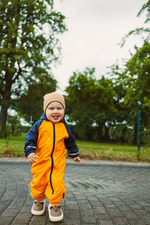 A cheerful toddler joyfully runs along a winding path in a vibrant yellow jumpsuit. The overcast sky adds a soft light to the scene filled with greenery.の写真素材