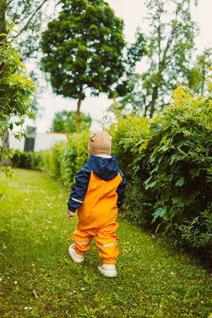 A young child walks down a winding garden path, wearing vibrant orange rain gear. Surrounded by greenery, the peaceful atmosphere invites exploration and adventure.の写真素材