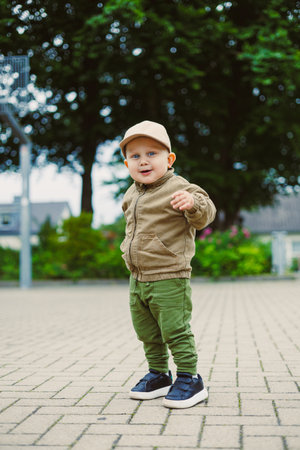 A cheerful young boy stands confidently in a park, wearing a cozy outfit and cap. He looks curious and adventurous, experiencing the beauty of nature on a bright day.の写真素材