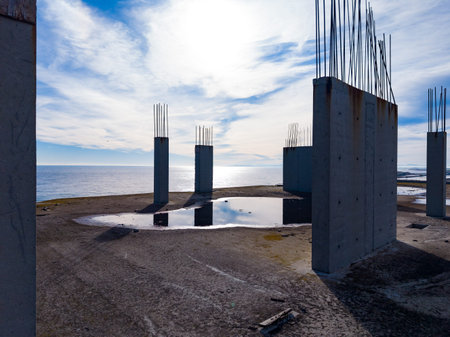 Concrete pillars stand on the ground at a construction site near the water. The sun shines above, casting light on the scene. The shore can be seen in the background.の写真素材