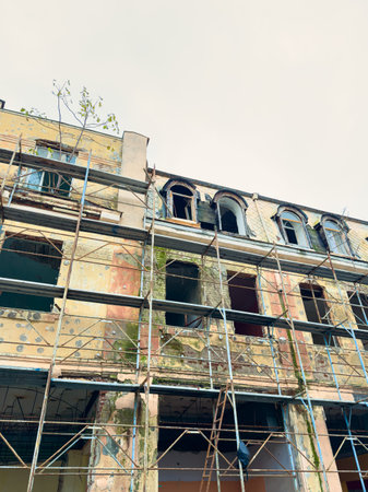 Scaffolding surrounds a dilapidated building, focusing on the upper level where workers are fixing the walls. Some windows are broken, showing signs of a long renovation process.の写真素材