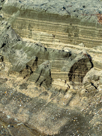 The shore displays layers of rock and sand formed over time. Different colors and textures are visible in the natural structure under bright sunlight.の写真素材