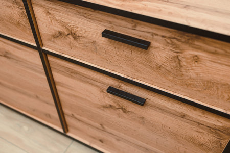 Close view of a wooden storage unit with two drawers and black handles. The surface shows natural wood patterns on a light floor in a bright space.の写真素材