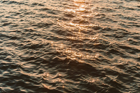 Light from the sun hits the surface of the water at a lake in the evening. Small waves and ripples create a sparkling effect across the water as it moves.の写真素材