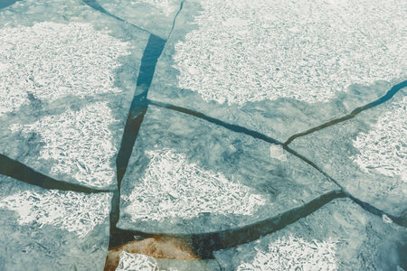 A frozen lake has various cracks and shapes in the ice. Some areas are clear while others hold snow. The patterns show the movement of water below the surface in the cold weather.の写真素材