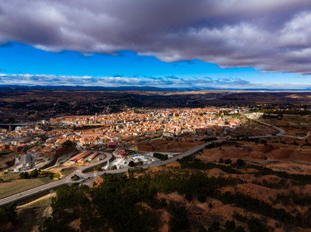 A view shows the city of Teruel from a high point. The layout of buildings is visible along with roads and green areas. The sky has clouds with sunlight shining through.の写真素材