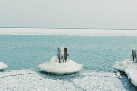 A pier made of wood sits on icy water. Snow covers parts of the pier while the water is frozen. The horizon is visible in the distance under a light sky.の写真素材