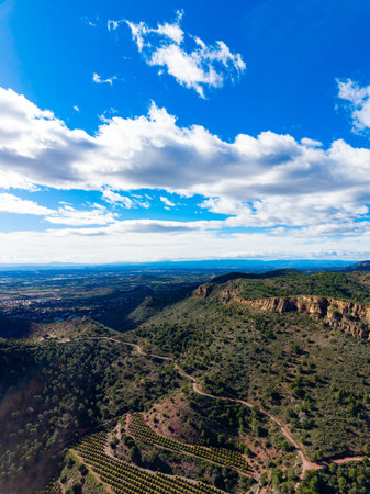 Hills stretch across the landscape under a blue sky with clouds. Vineyards are visible on the slopes. The view shows a mix of nature and farming. It is daytime and the scene is bright.の写真素材