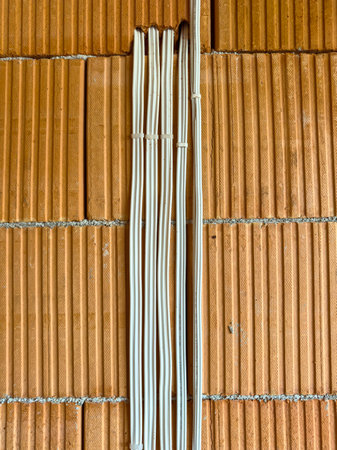 Electrical wiring is being secured to a textured brick wall. The site is busy with construction work occurring in the middle of the day.の写真素材