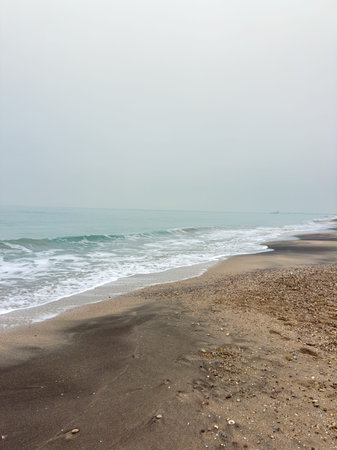 Waves gently roll onto the shore of a sandy beach under gray skies. The water appears calm and invites a sense of stillness. The scene captures the essence of a quiet coastal morning.の写真素材