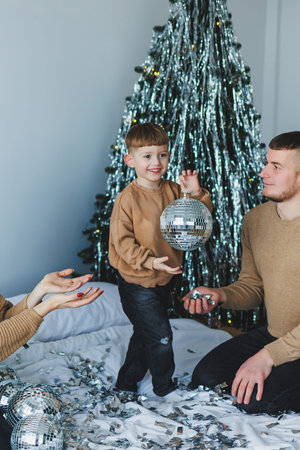 A child joyfully plays with a shiny disco ball, surrounded by loving family and festive decorations, capturing a delightful holiday atmosphere filled with warmthの写真素材