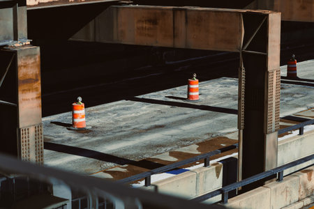 Workers focus on surface preparations at a construction area with traffic cones placed for safety. Sunlight casts shadows on the ground and barriers surround the site.の写真素材