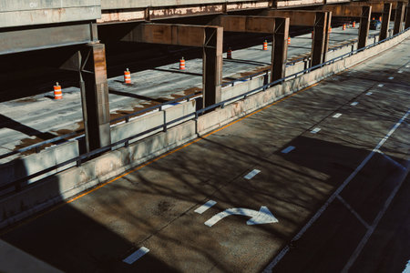 A highway shows empty lanes with construction cones placed along the sides. Shadows from structures above create patterns on the road. It is daytime and the area is quiet.の写真素材