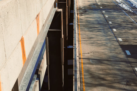 A view of a road under construction shows a secure structure above an empty lane. Shadows from nearby supports fall on the pavement. The setting is bright during the day.の写真素材