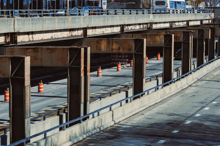 Workers are completing construction on a highway with traffic barriers in place. Vehicles can be seen on the road under the highway overpass during the day.の写真素材