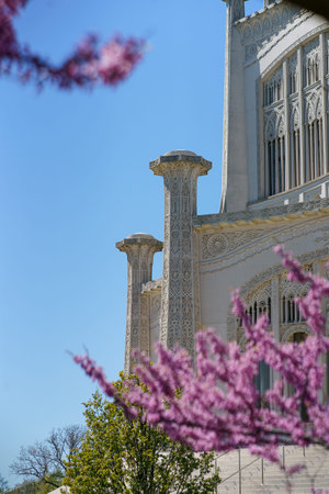 Bright pink flowers bloom in front of a historic building with intricate design under a clear blue sky. The scene shows the meeting of nature and architecture on a sunny day.の写真素材