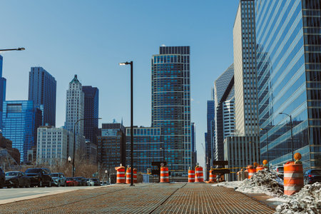 A view down a city street in Chicago features construction barrels and tall glass buildings under a clear blue sky on a bright sunny day. Cars line the street in the foreground.の写真素材