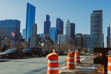 Traffic flows along the road surrounded by construction barriers. Tall buildings rise in the background under a clear blue sky. Flags wave gently in the light breeze.の写真素材