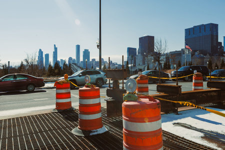 Construction barriers are set up on the road with cars driving by. The city skyline is visible in the background under clear blue skies during the day.の写真素材