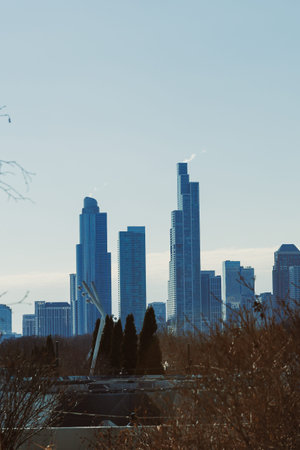 Many tall buildings rise in a city skyline against a blue sky. The scene shows urban life with...