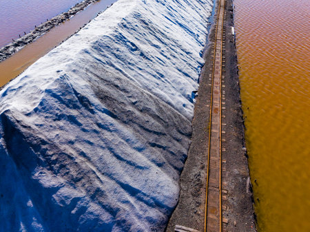 Large piles of salt sit beside two bodies of water. One area shows clear water while the other has...