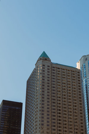 Tall buildings rise against a clear blue sky in the city. The structure on the right has a green roof and modern design. Light reflects from the glass windows.の写真素材