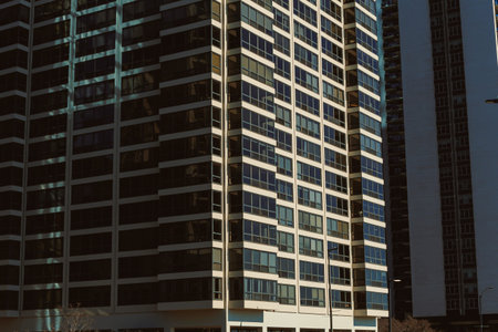A group of tall buildings with numerous windows are seen in an urban area. The sun reflects off the glass, showing the city architecture during daytime.の写真素材
