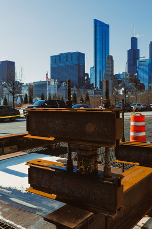 Workers are setting up a construction site with heavy equipment in front of tall buildings in Chicago. Cars move along the road while orange cones mark the area.の写真素材