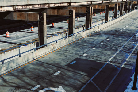 The scene shows a wide empty highway under a large structure. Traffic cones are placed along the road. Shadows from the structure are visible on the surface.の写真素材