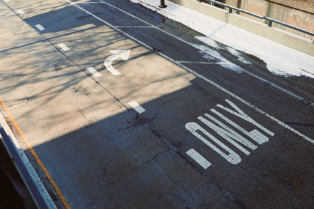Street scene displays lane markings indicating left turn only while shadows from a nearby structure fall on the asphalt during daytime.の写真素材