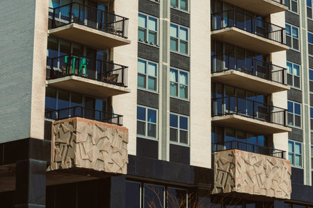 People can be seen using the balconies on a modern building. The structure features a unique wall...