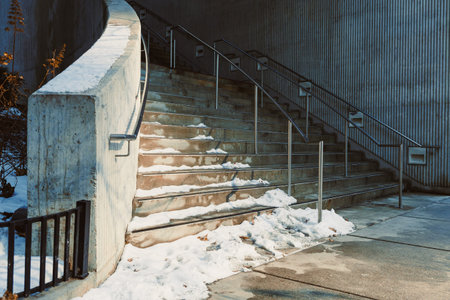 The stairs show snow on the steps and sides. Metal railings are present for safety. The scene is set in winter with some sunlight.の写真素材