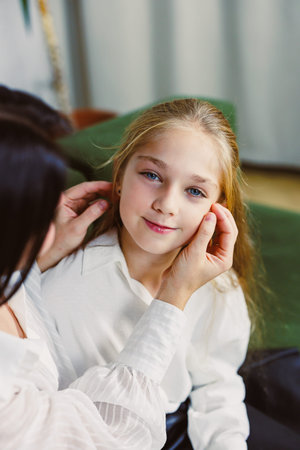 A mother gently adjusts her daughter's hair in a cozy living room setting. The child looks calm and happy as they prepare for a gathering.の写真素材